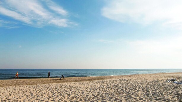 Ein Strand mit Sand, wenigen Personen und dem Meer.