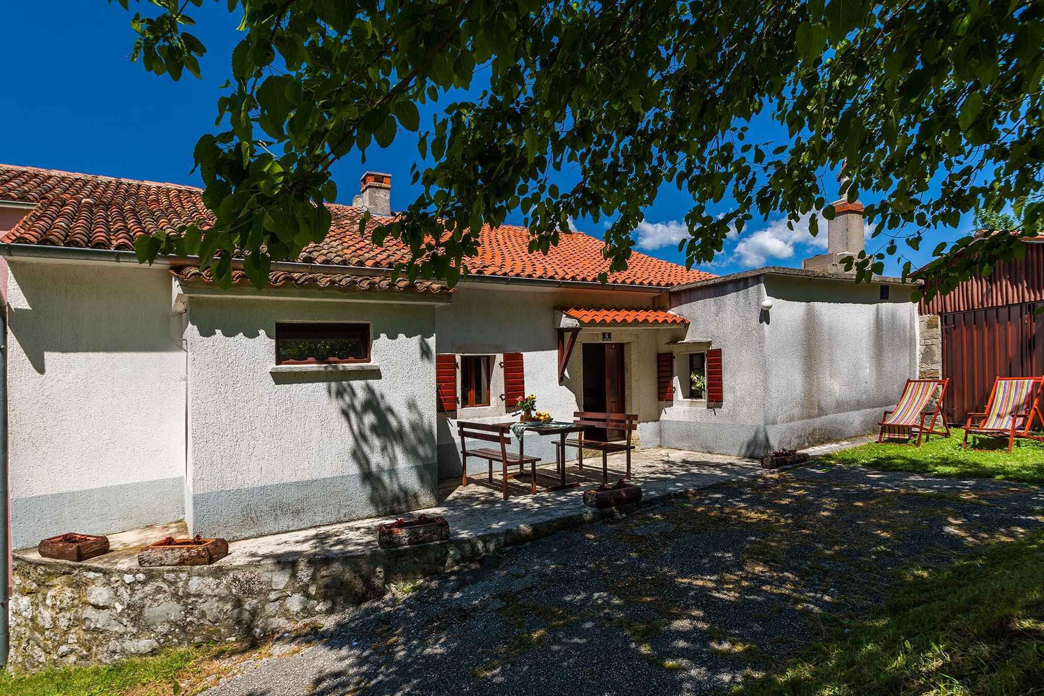 Une maison avec un toit en tuiles, un mur en pierre, une table en bois avec des chaises et un petit jardin.