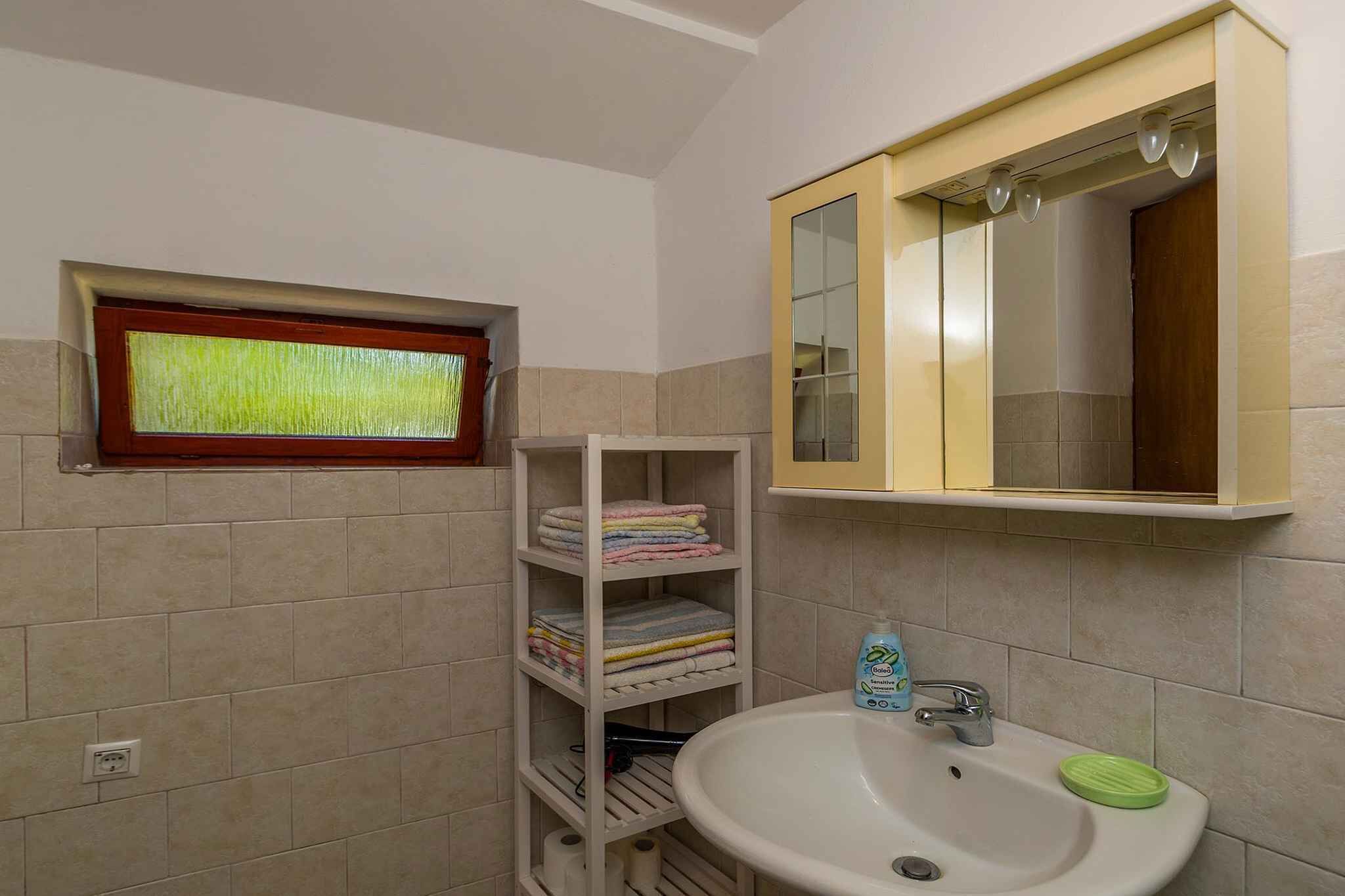 A bathroom with a window, a sink, a mirror, and a shelf with folded towels.