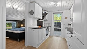 Kompakti keittiö, jossa on valkoiset kaapit, sisäänrakennettu uuni ja ikkuna, josta avautuu näkymä puutarhaan.