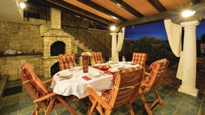 An outdoor dining area with a stone fireplace, wooden chairs, and a table set for four. - Amazing home in Izola (Izola)