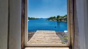 A view through a window of a wooden deck leading to a body of water, with a clear sky and distant land.