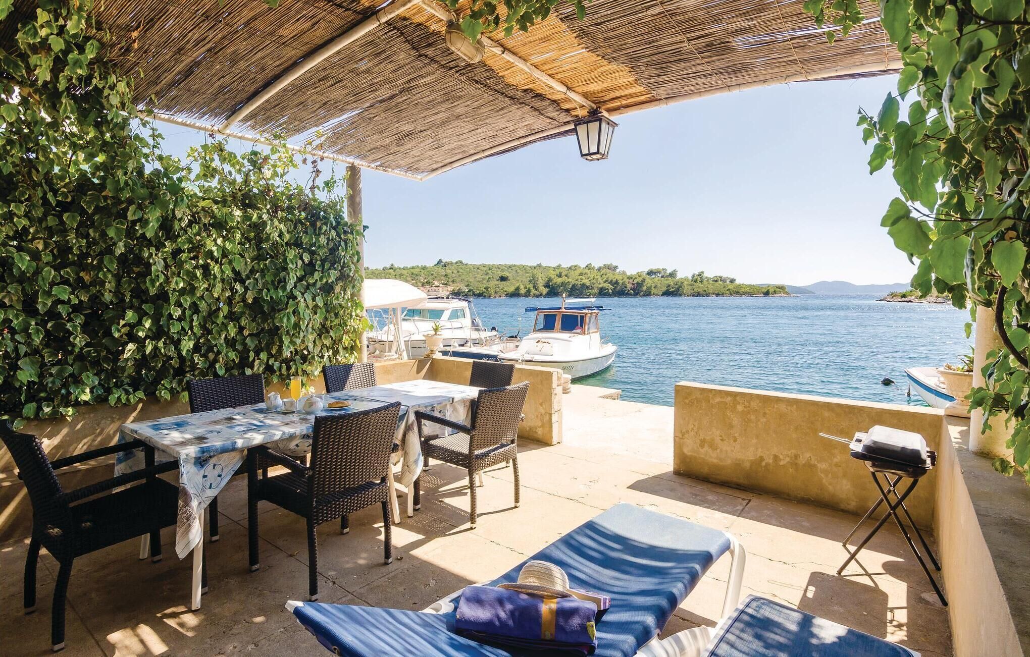 A covered outdoor seating area with a table and chairs, overlooking a body of water with boats.