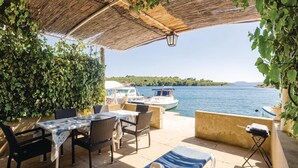 A covered outdoor seating area with a table and chairs, overlooking a body of water with boats.