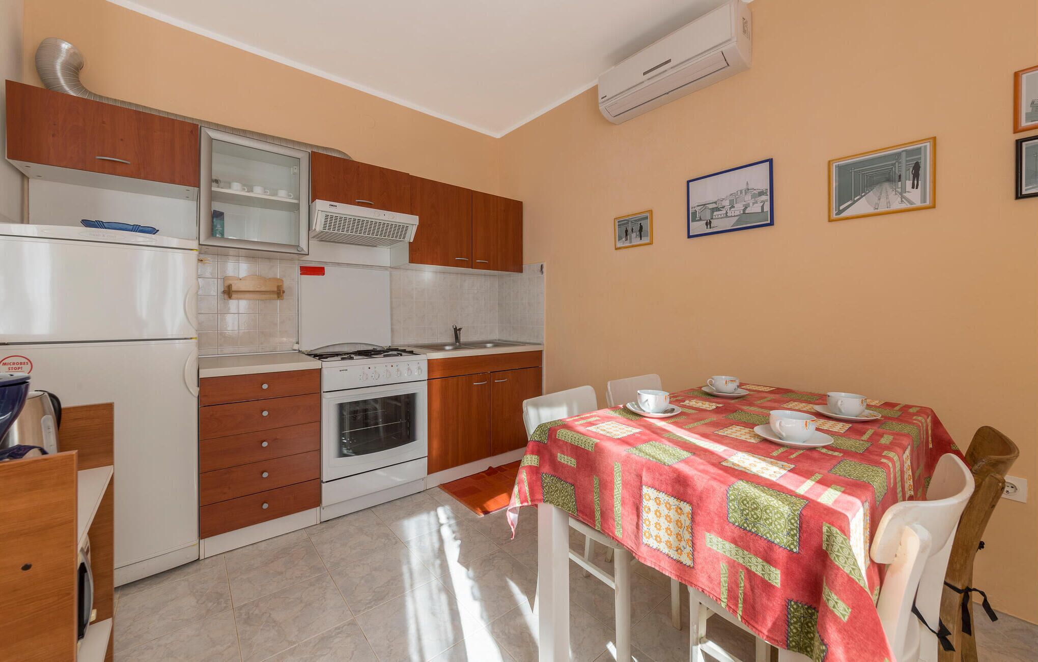 A compact kitchen with a gas stove, oven, and a refrigerator. There is a dining table with a red tablecloth and white chairs.