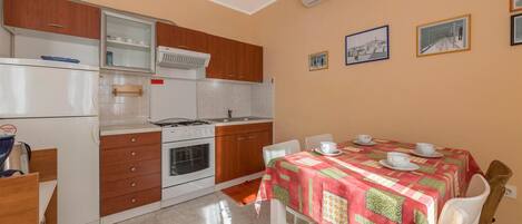 A compact kitchen with a gas stove, oven, and a refrigerator. There is a dining table with a red tablecloth and white chairs.
