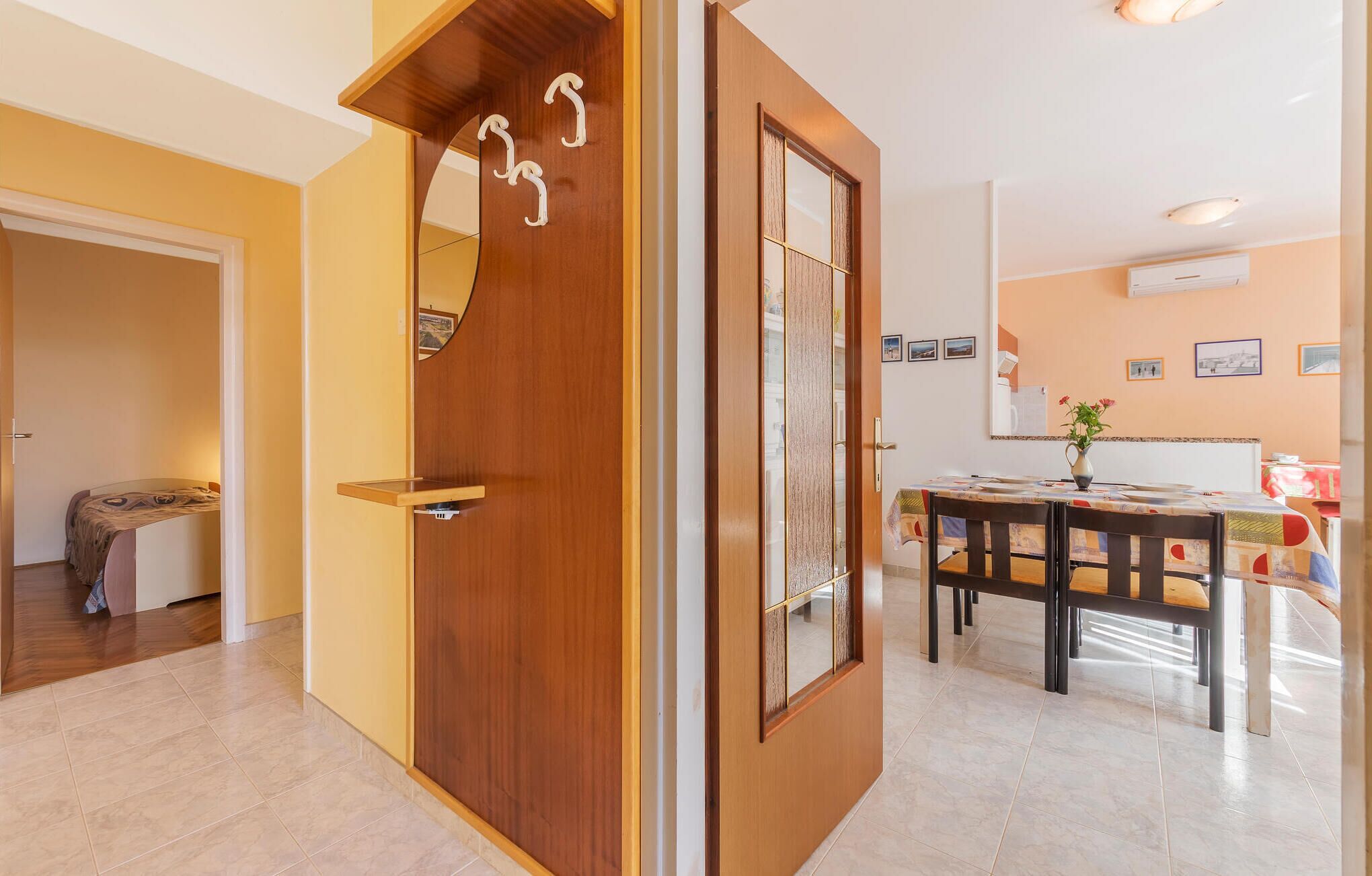 Un interior modern amb una porta de fusta, una zona de menjador amb taula i cadires, i una cuina al fons.