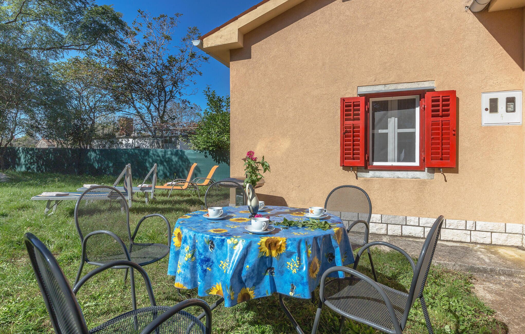 An outdoor seating area with a table covered in a blue floral tablecloth, surrounded by metal chairs.