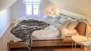 Un dormitorio acogedor con una cama de madera, ropa de cama blanca, un edredón gris y una mesita de noche con una lámpara.