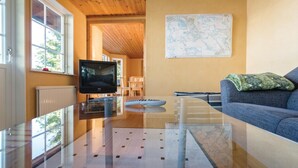 Un salon moderne avec une table basse en verre, un téléviseur, une carte accrochée au mur et un canapé recouvert d’une couverture.