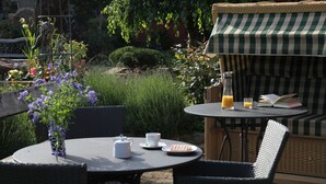 An outdoor patio with wicker furniture, a table with a book, a bottle, and a cup. - 6 Kräuterkammer 5 Stars - Ferienwohnanlage Alte Molkerei 5 Stars (Rankwitz)