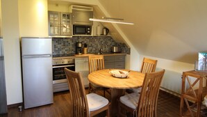 A compact kitchen with a refrigerator, oven, microwave, and a small dining area with a wooden table and chairs. - 6 Kräuterkammer 5 Stars - Ferienwohnanlage Alte Molkerei 5 Stars (Rankwitz)