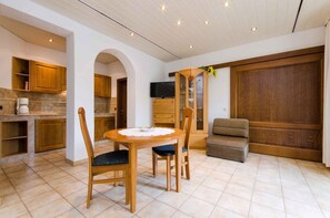 Cozy living space with a kitchen and seating area, featuring a flat-screen TV and a round table with two chairs and a bench.
