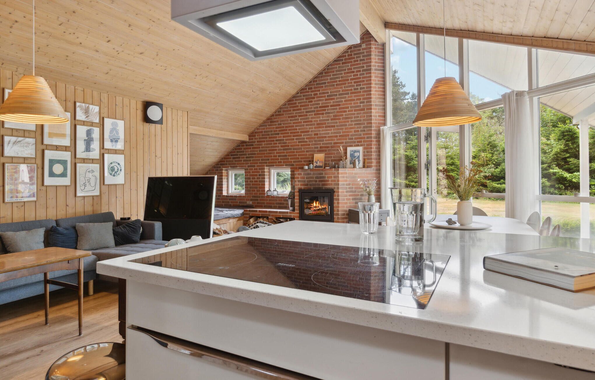 A cozy living room with a fireplace, wooden walls, and a large window offering a view of the outdoors.
