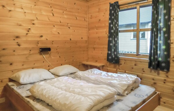 Une pièce de cabane en bois comprenant un lit, une petite table et une fenêtre avec des rideaux.