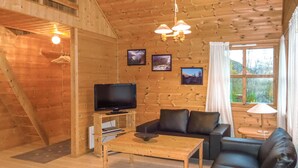 A cozy cabin interior with a wooden interior, a television on a wooden stand, a sofa, a coffee table, and framed pictures on the wall. - 2 bedroom beach front home in Vallavik (Vallavik)