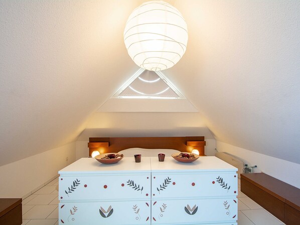 A room with a white chest of drawers, a wooden headboard, and a ceiling light fixture.