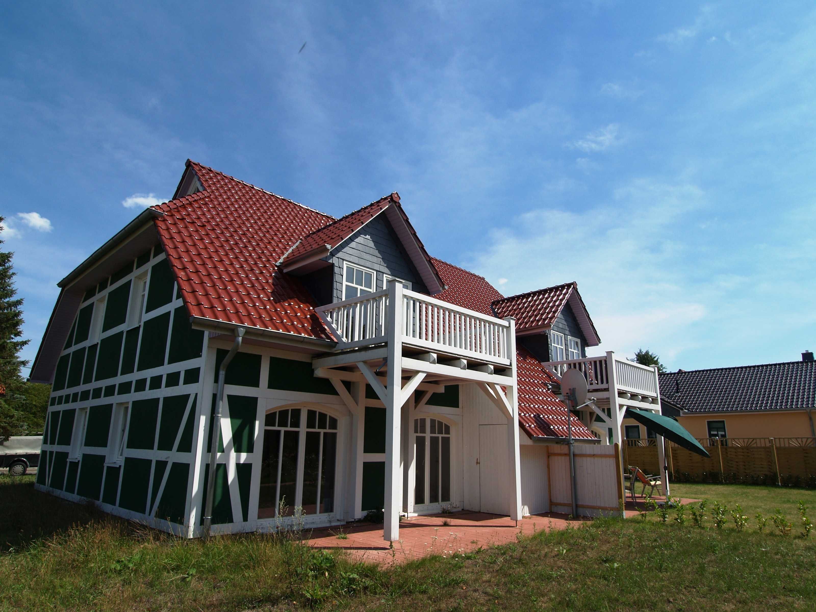 Ein zweistöckiges Haus mit rotem Ziegeldach, weißem Zierwerk und einem Balkon.