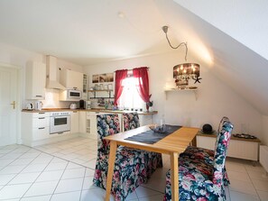 A compact kitchen with white cabinets, a microwave, and a dining area with floral chairs and a wooden table.