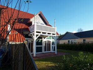 Ein zweistöckiges Haus mit rotem Ziegeldach, einem Balkon und einem Garten.