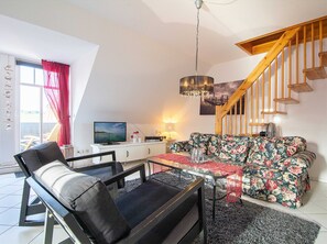 A living room with a sofa, a dining table, a TV, and a staircase.