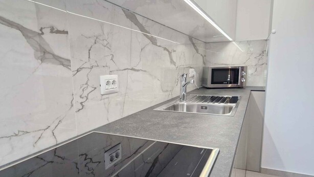 Una cocina moderna con encimeras de mármol, un fregadero de acero inoxidable y un microondas integrado.