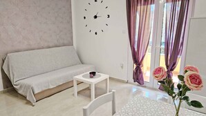 Una sala de estar moderna con sofá, una mesita, un reloj y un ventanal con cortinas.