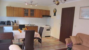 Una sala de estar con sofá, una mesa de centro y un comedor con mesa y sillas. Hay una zona de cocina con armarios y electrodomésticos.