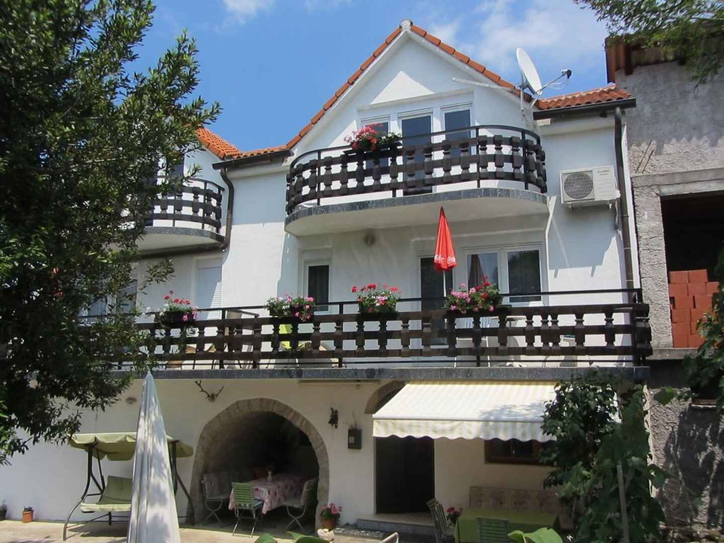 A two-story building with a balcony, a covered outdoor seating area, and a small archway entrance.