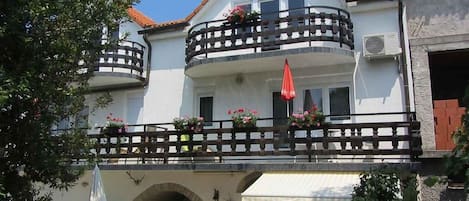 A two-story building with a balcony, a covered outdoor seating area, and a small archway entrance.
