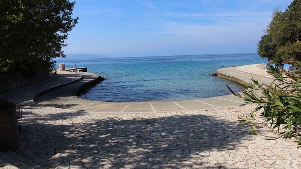 Un sendero de piedra que conduce a una zona frente al agua, con un pequeño muelle y escalones para acceder al agua.