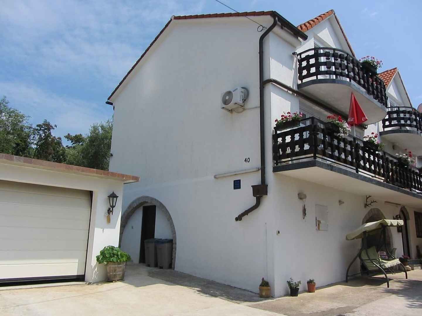 A white building with a balcony, a garage, and potted plants.