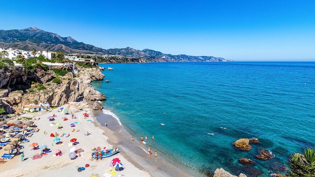 A beach with clear blue water, rocky coastline, and a town in the background. - Cozy home in Nerja with WiFi (Nerja)