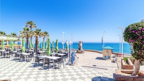 A seaside patio with tables and chairs, a statue, and a view of the ocean. - Cozy home in Nerja with WiFi (Nerja)