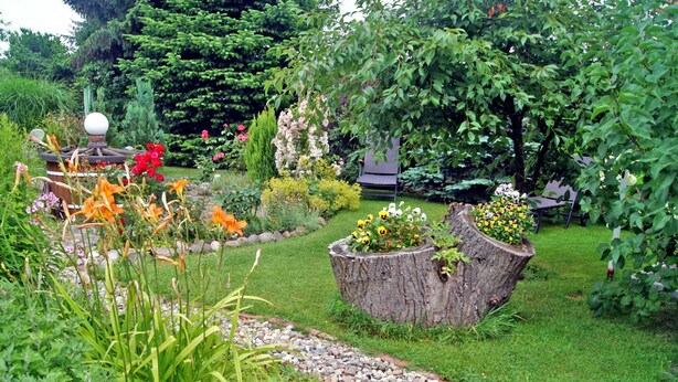 A garden with a variety of plants and flowers, a wooden bench, and a decorative stone structure. - Vacation cottage Ursula - Holiday cottage (Malchow)
