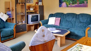 A living room with a blue sofa, a television, a bookshelf, and a painting on the wall. - Vacation cottage Ursula - Holiday cottage (Malchow)