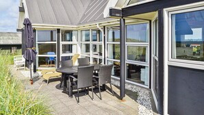 Ett modernt hus med ett vinterträdgård, en utomhusplats med sittmöbler och stora fönster.