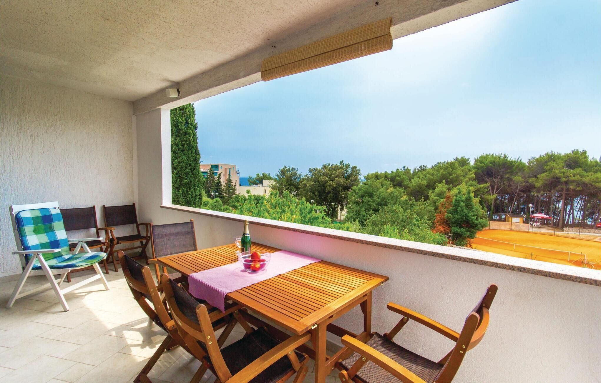 Un balcón con mesa y sillas de madera, vista al mar y una fila de árboles.