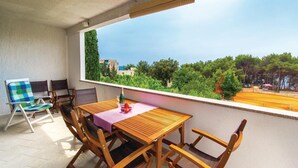 Un balcón con mesa y sillas de madera, vista al mar y una fila de árboles.