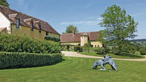 A yellow building with a tiled roof, surrounded by well-maintained hedges and a grassy lawn.