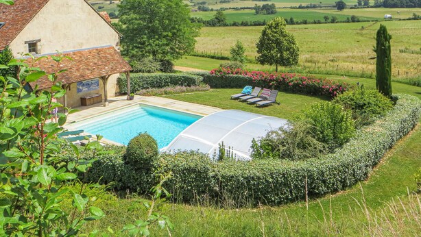 A pool area with a house, a covered seating area, and a view of the countryside.