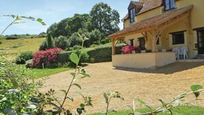 A house with a covered porch, a gravel driveway, and a garden with pink flowers and green shrubs.