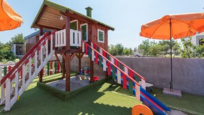 A wooden playhouse with a slide, surrounded by artificial grass and a concrete wall. - Gorgeous home in Brodarica (Brodarica)