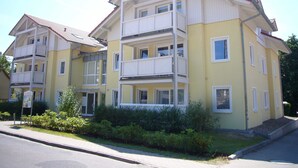 Ein mehrgeschossiges Wohngebäude mit Balkonen, einem roten Dach und einem gepflegten Garten.