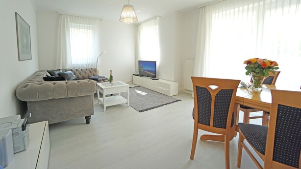 Ein modernes Wohnzimmer mit einer Couch, einem Fernseher, einem Esstisch, Stühlen und einer dekorativen Vase.