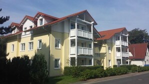 Ein mehrgeschossiges Wohnhaus mit rotem Ziegeldach, Balkonen und einem gepflegten Rasen.