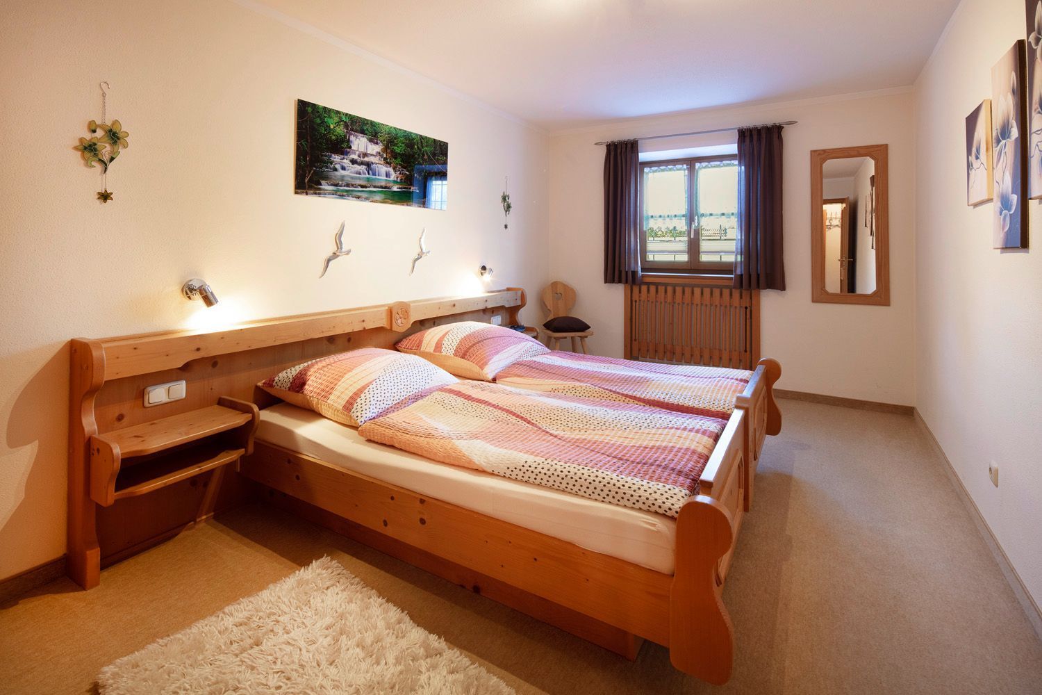 Een slaapkamer met een houten bed, een raam met gordijnen, een aan de muur hangend schilderij en een klein nachtkastje.