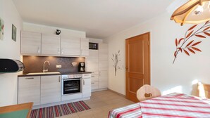 Een kleine keuken met een magnetron, oven en koffiezetapparaat, een houten deur en een bed met een gestreept dekbed.