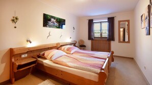 Een slaapkamer met een houten bed, een raam met gordijnen, een aan de muur hangend schilderij en een klein nachtkastje.