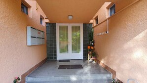 A building entrance with a double door, a small step leading up, and a wall-mounted electrical box.